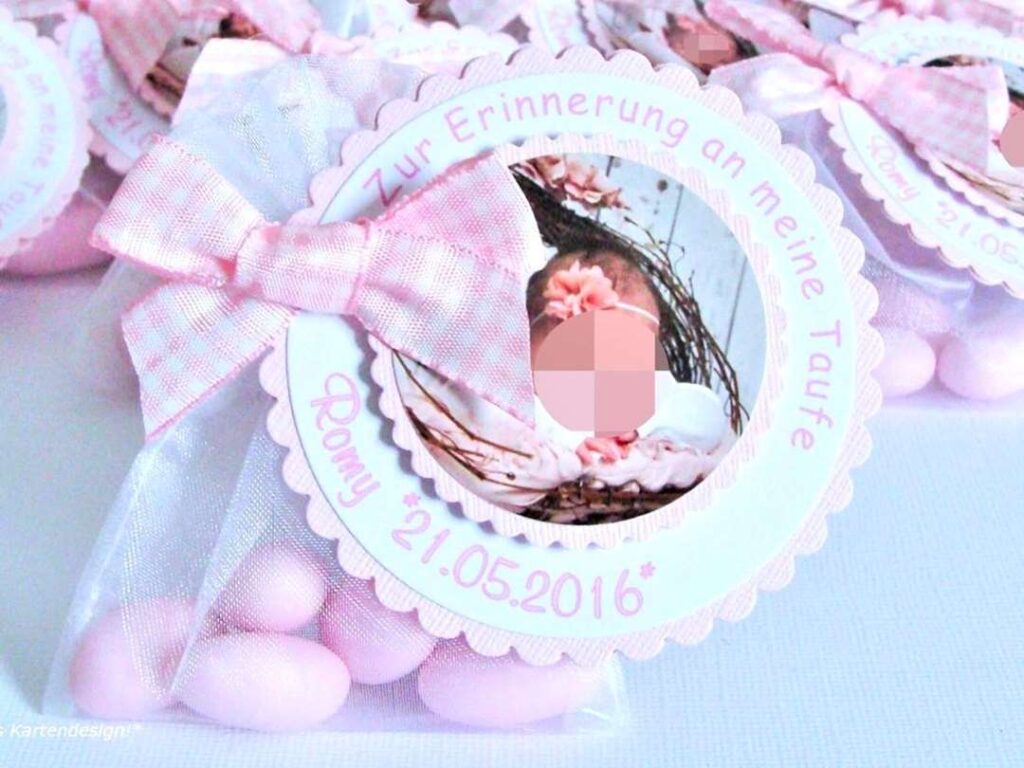 Gastgeschenk Mandelsaeckchen zur Taufe in rosa. Rund gewellter Anhaenger ist mit Taufdaten personalisiert. Mittig darin ist auf einem kleineren gewellten Label ein Foto des Taeufling angeordnet. Befestigt ist der Anhaenger mit einer rosa karierten Schleife, auf einem Organzasaeckchen in weiss, befuellt mit fuenf rosa Taufmandeln. Mandelspruch befindet sich rueckseitig. Design Lovely Times © KARTEN-DESIGN.at Nicki Heß