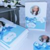 Handgefertigtes weißes Kirchenheft - Design: Sweet Baby, in Wunschfarbe Blau mit Babyfoto und Namensanhänger. Taufheft im geprägten Design mit Satin-Schleife in Baby-Blau und personalisierten Text. © KARTEN-DESIGN.at