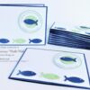 Kommunionseinladung Fische – handgefertigte Einladungskarte zur Erstkommunion mit christlichem Fisch-Motiv und Personalisierung in Wunschfarbe blau und gruen. Klappkarte 15 x 11 cm mit weißer Punkte-Praegung. © KARTEN-DESIGN.at Nicki Heß Salzburg