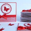 Taufeinladung "Sweet Circle" in Rot personalisiert mit 3D-Schmetterling und Pünktchenband in Baby-Rot. Taufkarte mit Personalisierung, Taufspruch und Babyfüsschen. © KARTEN-DESIGN.at
