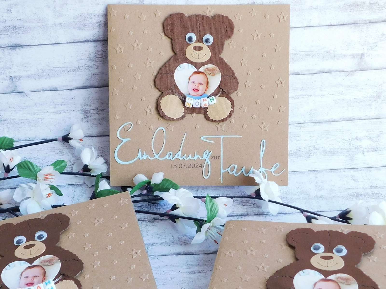 Taufeinladung aus Kraftkarton mit individueller Sternen-Prägung, süßem Teddy-Bären mit Kulleraugen & Foto eines Babys in Herzform darin. Kleine bunte Buchstabenwürfel mit dem Namen des Babys zieren den Teddy. Darunter ist der Schriftzug "Einladung zur Taufe" aus farbigen blauen Papier gestanzt und auf der Taufkarte befestigt. © KARTEN-DESIGN.at | Nicki Heß