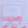 Weiße Taufeinladung im Format 13,5 x 13,5 cm, mit farbigen Hintergrund in Wunschfarbe Rosa, darauf ein weiß geprägtes Papier mit Schmetterling-Prägung. Mittig ein oval geschwungenes Textlabel mit Personalisierung. Ein rosa Satinband im unteren Bereich ziert die Taufkarte. Design: Lovelycard © KARTEN-DESIGN.at Nicki Heß